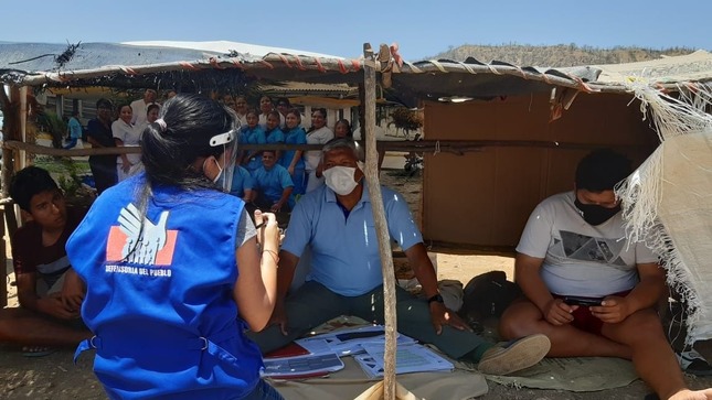 Representante de Defensoría Perú entrevistando a 3 ciudadanos que están sentados bajo carpa improvisada. 