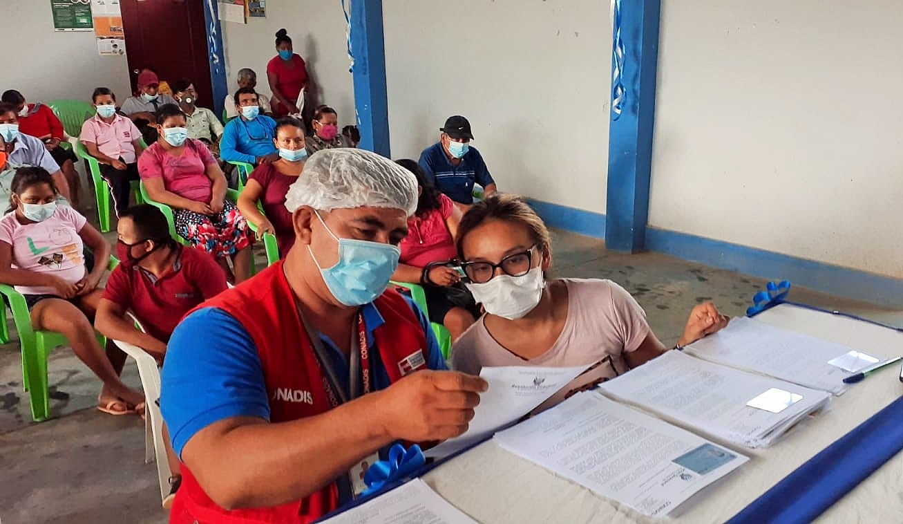 Un hombre entregando las resoluciones y carnet del Conadis en e distrito de honoria, una mujer recibe todo.
