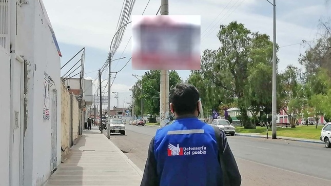 Comisionado de la Defensoría del Pueblo parado frente a un poste con propaganda electoral