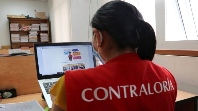 Imagen JPG de colaborador de la Contraloría en los interiores de una oficina, sentado y revisando contenido del programa Auditores Juveniles.