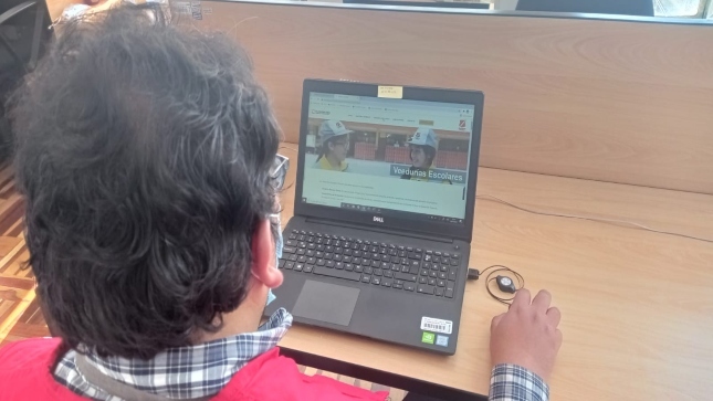 Imagen JPG de colaborador de la Contraloría en los interiores de una oficina, sentado y revisando contenido sobre el programa Auditores Juveniles.