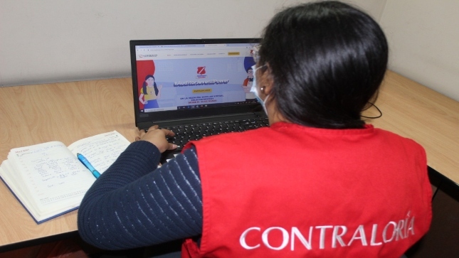 Imagen JPG de colaborador de la Contraloría en los interiores de una oficina, sentado y revisando contenido del programa Auditores Juveniles.