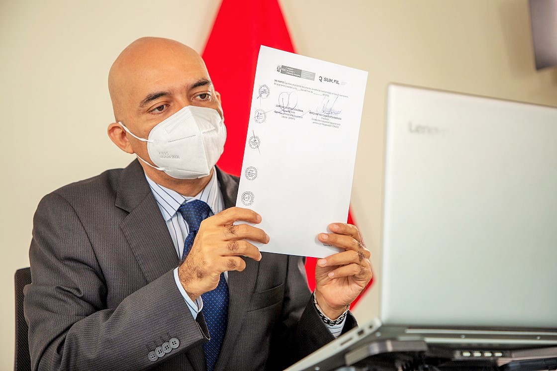 En la foto el presidente del Conadis Marco Antonio Gamarra La Barrera esta sentado y muestra el convenio firmado.