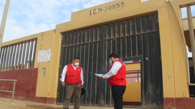 Imagen JPG de dos colaboradores de la Contraloría en los exteriores de la puerta principal de la institución educativa en el marco de la supervisión en la entrega de tablets a escolares y docentes.