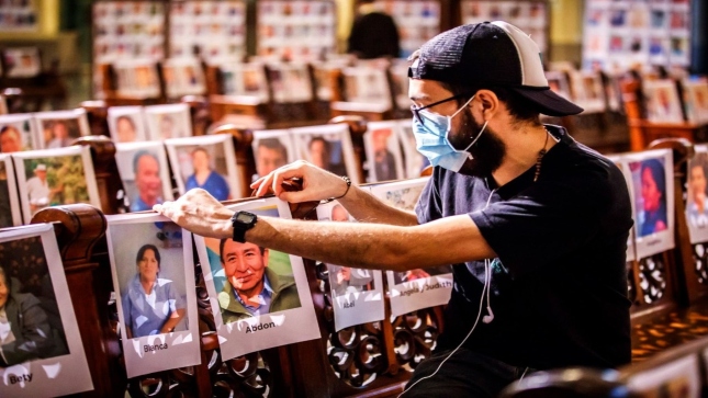 .Imagen JPG de un hombre observando varias fotografías de personas fallecidas por la COVID-19.