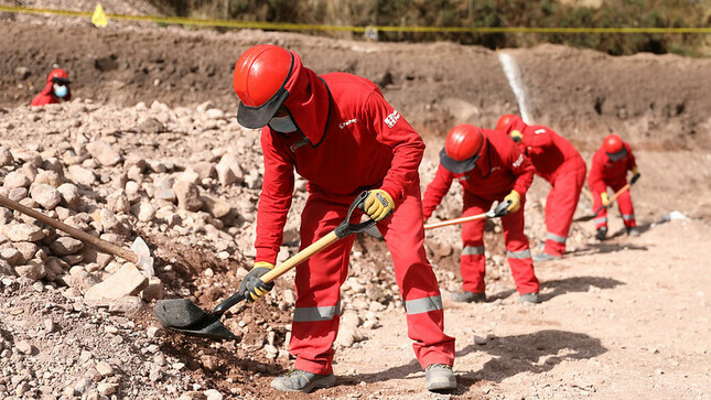 Hombres trabajando .Tienen uniforme de color rojo y estan con sus lampas limpiando le piso.