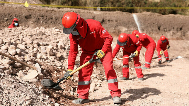 Hombres trabajando .Tienen uniforme de color rojo y estan con sus lampas limpiando le piso.