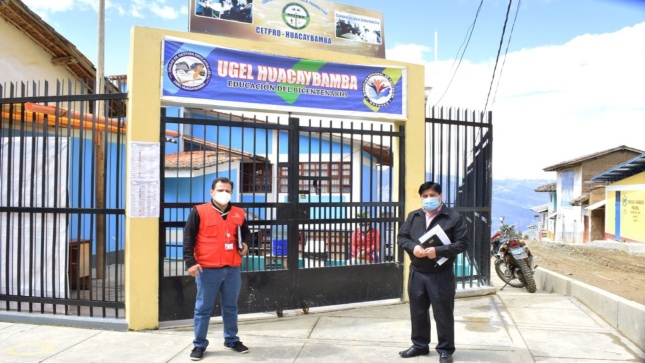 Imagen JPG de colaborador de la Contraloría junta otra persona paradas en los exteriores de la puerta principal y parte de la fachada de la Dirección Regional de Educación de Huánuco y del Ministerio de Educación (Minedu).