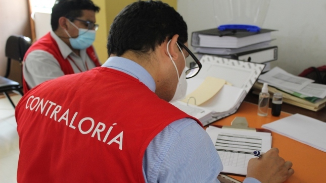 Imagen JPG de dos colaboradores de la Contraloría, sentados en sillas y revisando archivos y papeles en un escritorio, dentro de las instalaciones de la Municipalidad Distrital de Nepeña.