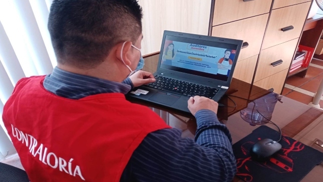 Imagen JPG de colaborador de la Contraloría sentado en una silla en el interior de su oficina y mirando información del programa Auditores Juveniles desde su laptop.