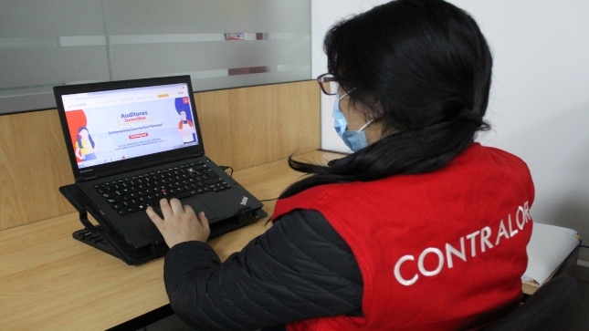 Imagen JPG de colaboradora de la Contraloría sentada revisando información sobre el programa Auditores Juveniles en su laptop.