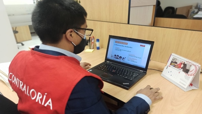 Imagen JPG de colaborador de la Contraloría sentado en su escritorio y revisando en su laptop información sobre el curso virtual "El control social en tus manos" Huancavelica.