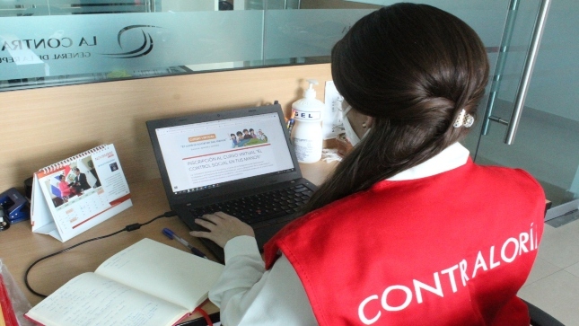 Imagen JPG de una colaboradora de la Contraloría sentada en un escritorio y revisando información en su laptop sobre el Curso virtual “El control social en tus manos” Cajamarca.