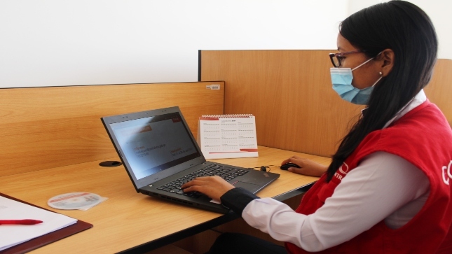 Imagen JPG de colaboradora de la Contraloría sentada en su escritorio revisando información sobre el curso virtual "El control social en tus manos" Moquegua en su laptop.
