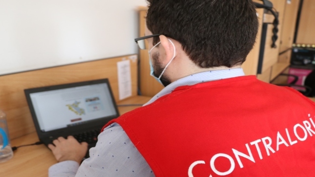 Imagen JPG de colaborador de la Contraloría sentado, trabajando con su laptop en su escritorio.