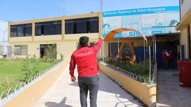 Imagen JPG de colaborador de la Contraloría señalando la fachada y puerta principal de Dirección Regional de Salud Moquegua