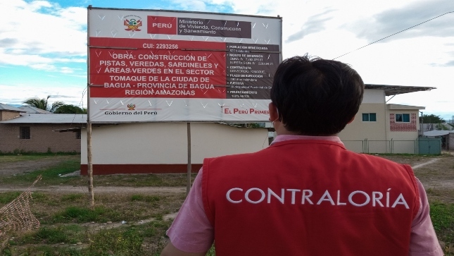 Imagen JPG de colaborador de la Contraloría mirando un cartel con información del proyecto de obra de construcción en la región Amazonas.