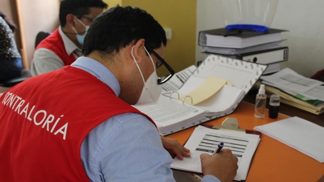 Imagen JPG de dos colaboradores de la Contraloría sentados en un escritorio, uno revisando un archivo con papeles de normativas en los Estudios de Ingeniería Básica para las obras que ejecuta la Autoridad para Reconstrucción con Cambios y el otro escribiendo. 
