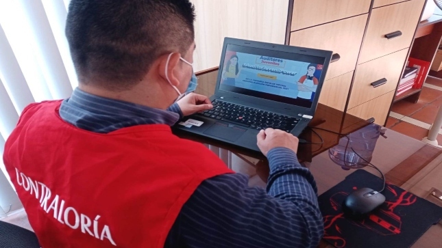 Imagen JPG de colaborador de la Contraloría sentado en su escritorio mirando revisando información en su laptop sobre el programa Auditores Juveniles.
