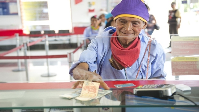 Imagen JPG de una mujer adulta mayor cobrando dinero en un banco por el del programa Pensión 65.