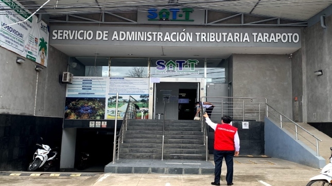 Imagen JPG de colaborador de la Contraloría señalando la fachada del Servicio de Administración Tributaria (SAT) de Tarapoto.
