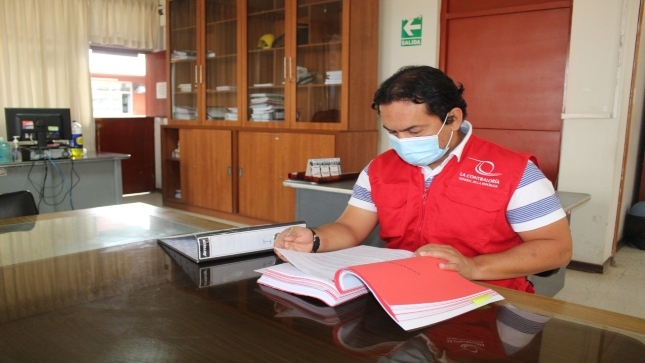 Imagen JPG de colaborador de la Contraloría sentado en su escritorio revisando documentos.