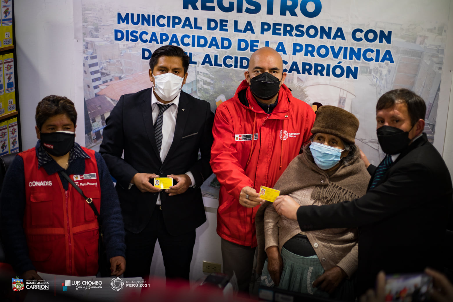 Participan el Presidente del Conadis, Eco. Marco Antonio La Barrera, Alcalde de la provincia Daniel Alcides Carrión, Juan Luis Chombo Heredia y personal que están entregando los carnet de discapacidad. Se muestran los carnet de color amarillo y celeste.