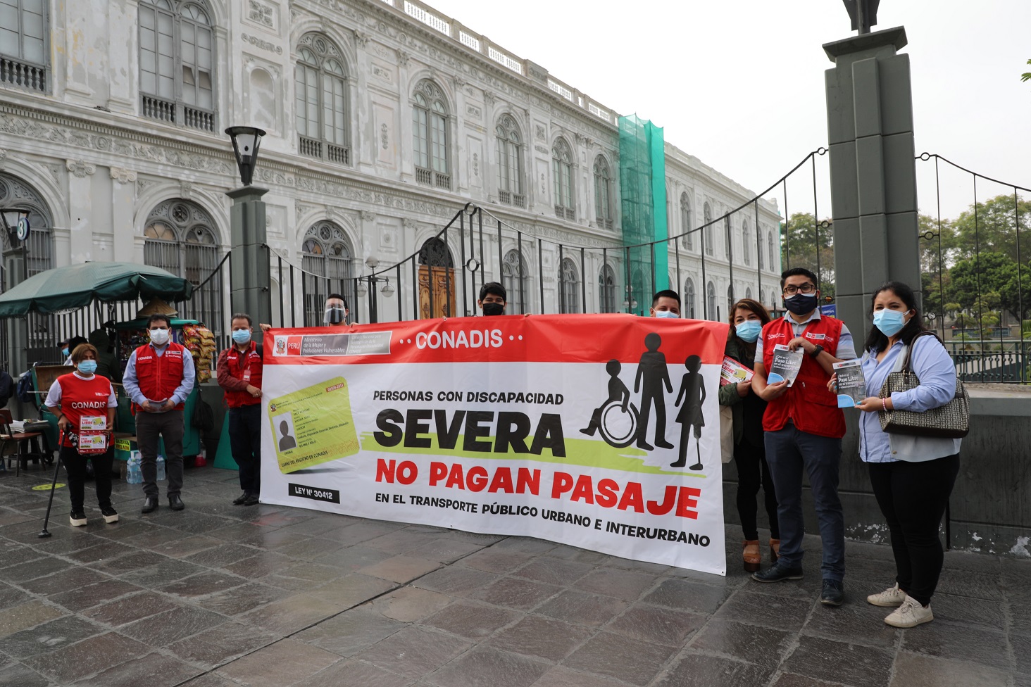 Grupo de personas muestran un banderola del Pase Libre, están en la calle en una activación de sensibilización.