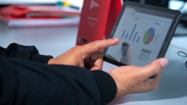 Imagen referencial de las manos de una persona sosteniendo una tablet en cuya pantalla se aprecian cifras y estadísticas.