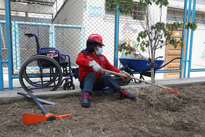 Persona con discapacidad motora sentada en el piso haciendo el mejoramiento de jardines