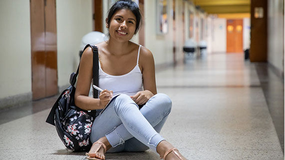 Becaria del Pronabec en pasillo de una universidad mira a la cámara