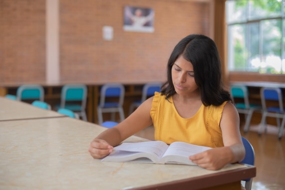 Joven estudiante leyendo un libro en una biblioteca.
