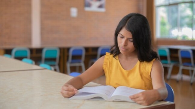 Joven estudiante leyendo un libro en una biblioteca. 