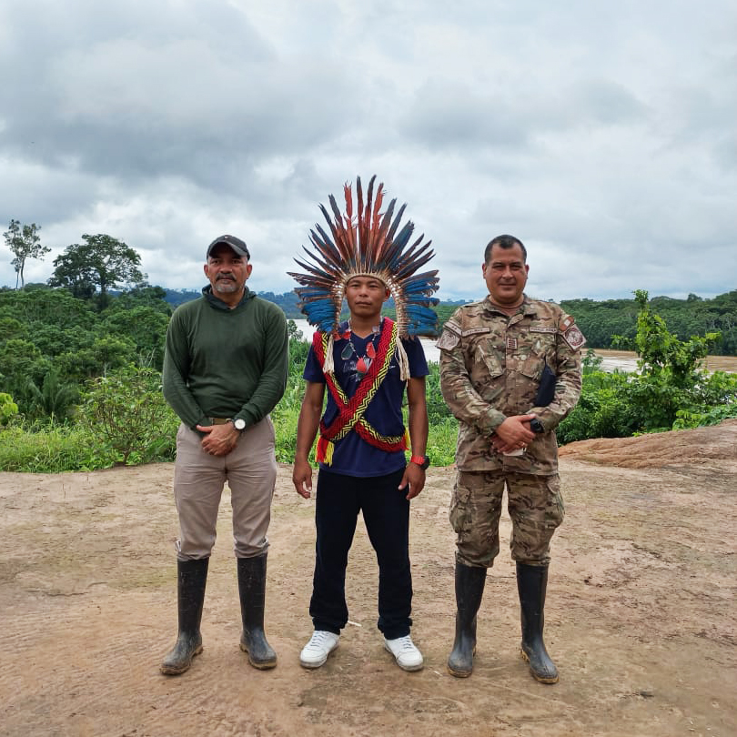 Fotografía del presidente y un miembro del ejército con un joven que tiene en la cabeza una vincha de plumas