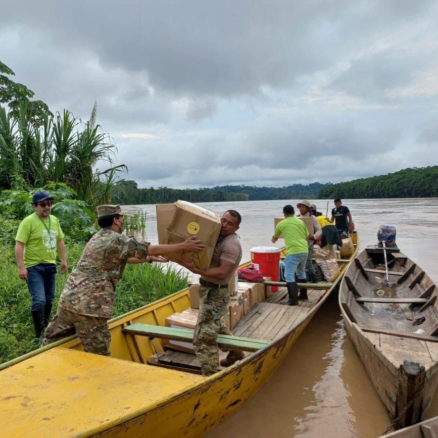 Fotografía de miembros de las fuerzas armadas desembarcando donaciones de unos botes al borde del río