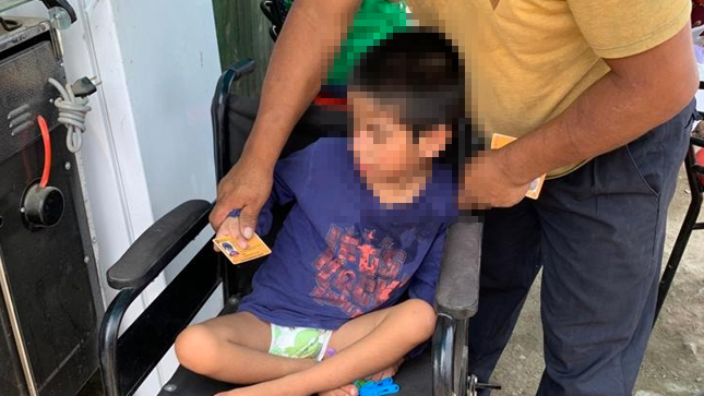 Fotografía de un niño en silla de ruedas mostrando su carnet de conadis color amarillo