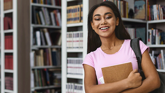 Estudiante afro mira a la cámara mientras abraza un libro