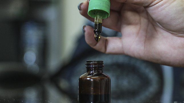 Una mano tiene un gotero de donde cae cannabis en gotas.