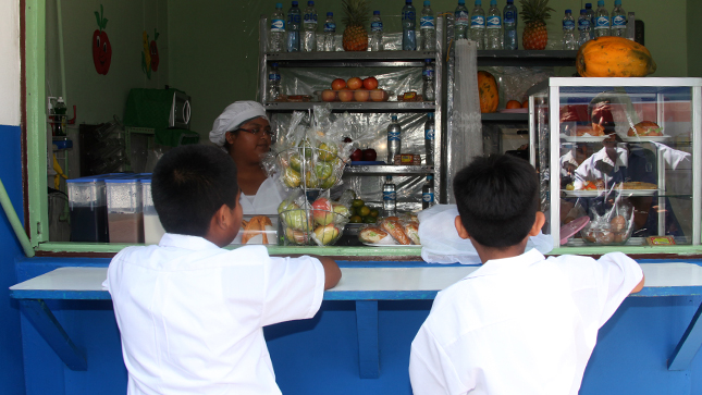 En la foto aparecen dos niños comprando en un quiosco donde hay frutas.