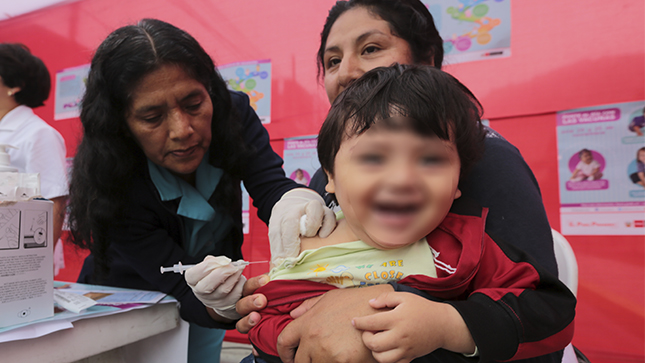 Una enfermera coloca la vacuna a un bebé que está en los brazos de su madre.