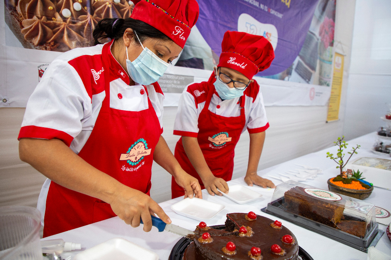 Madre e hijo cortado una tota de chocolate sobre una mesa que tiene varios adornos.
