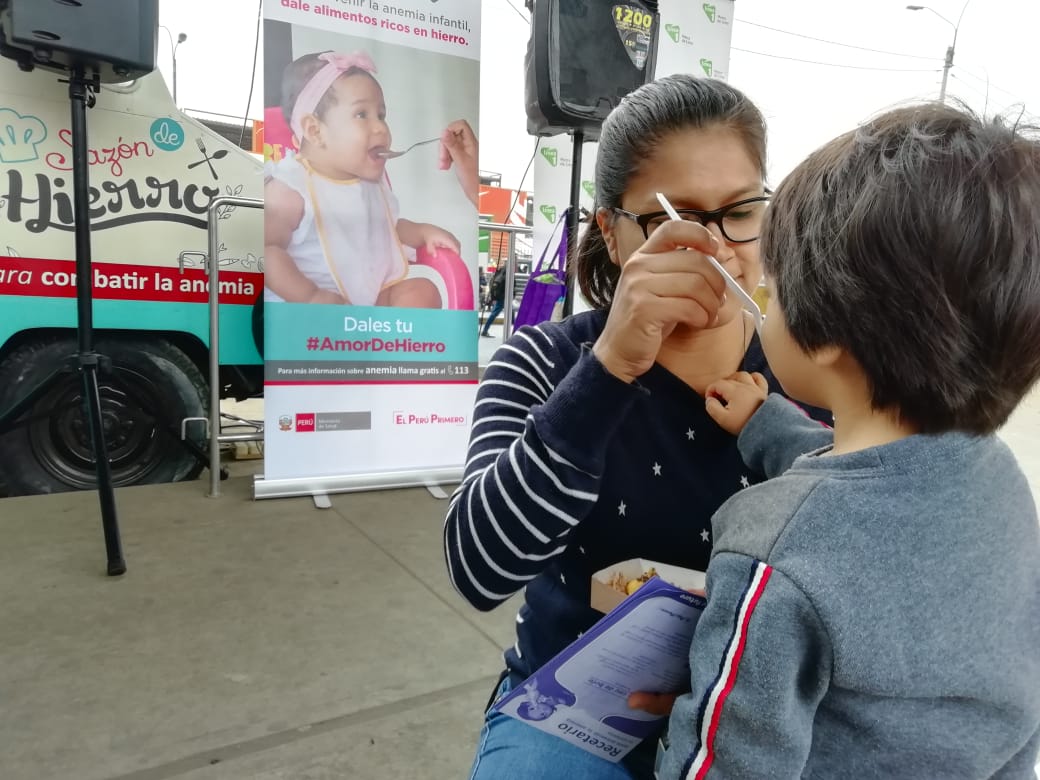 En foto se ve a una madre dando de comer a su niño delante del camión Food Truck