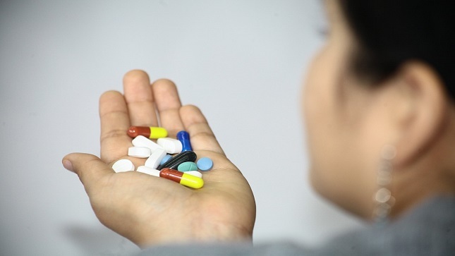 En la foto se ve a una mujer con pastillas en la mano.