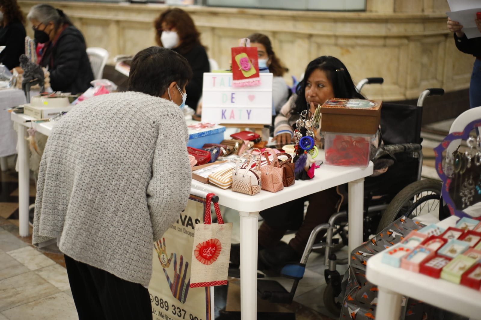 Personas con discapacidad de diversos organizaciones exponiendo su productos sobre una mesa y personas comprando , en la sede del Congreso de la República en sus instalaciones del edificio Luis Alberto Sánchez, en el Cercado de Lima.