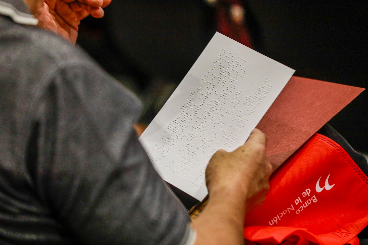 Imagen de una hoja en blanco con escritura braille sostenida por un mano.