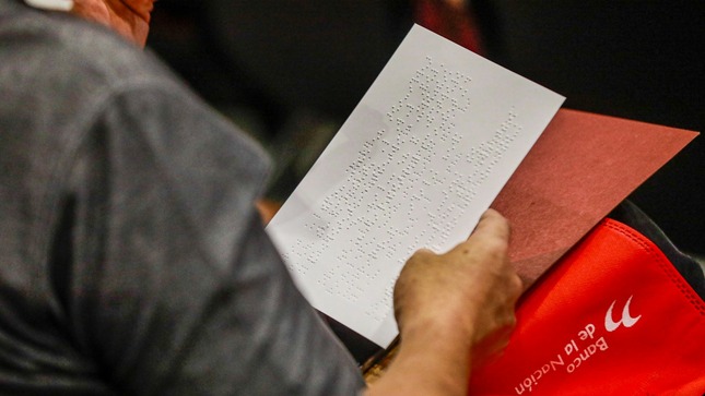 Imagen de una hoja en blanco con escritura braille sostenida por un mano.