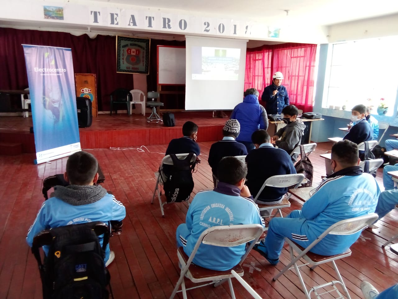 En la imagen está los estudiantes de espalda mirando a la pizarra