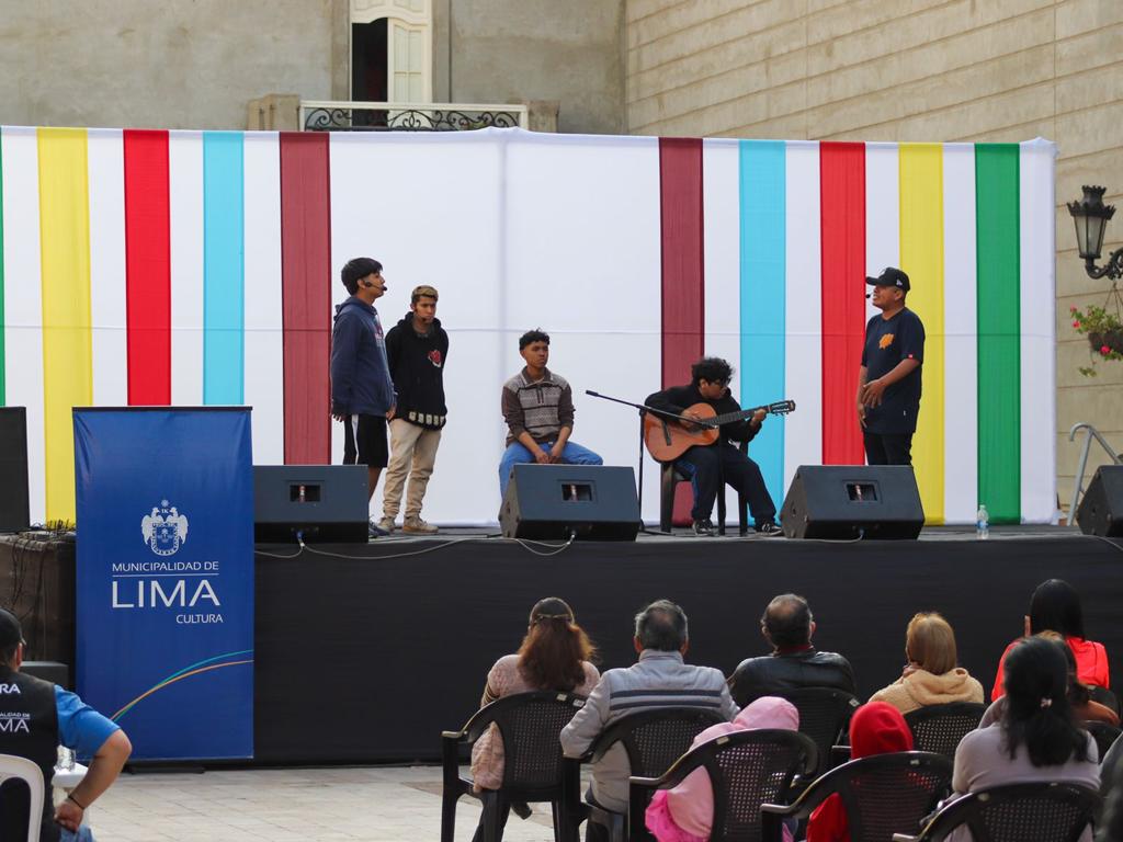 Jóvenes músicos tocando guitarra y cajón en escenario.