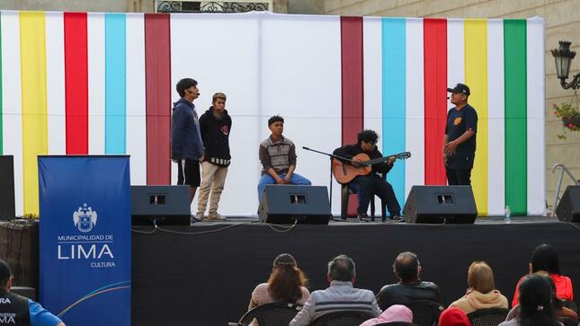 Jóvenes músicos tocando guitarra y cajón en escenario.