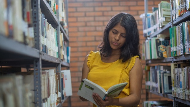 Joven talento del Pronabec revisando un libro en la biblioteca.